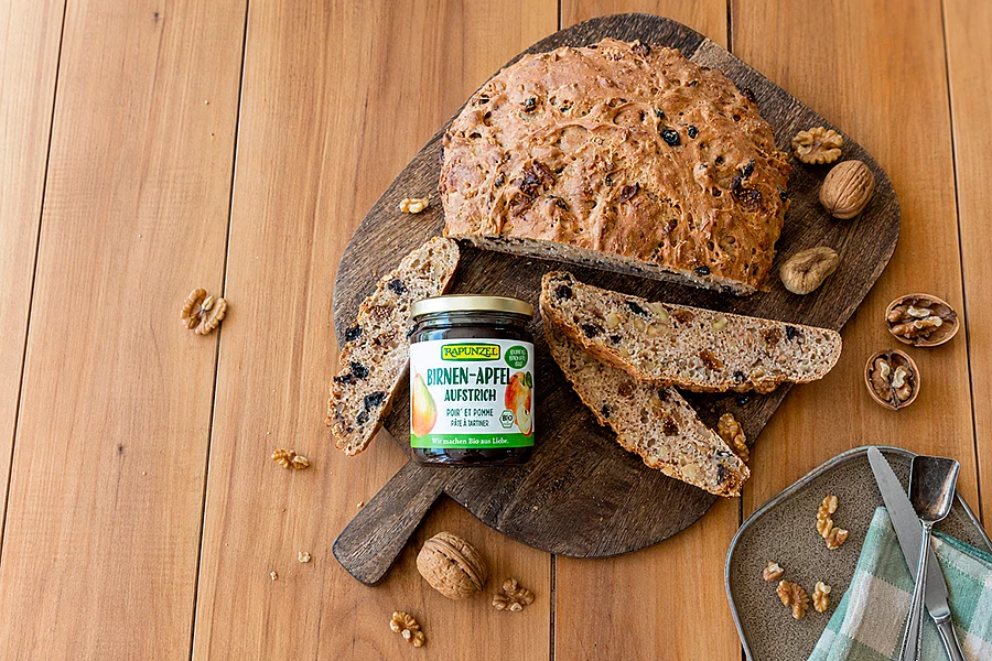 Ein Glas Apfel-Birnen-Kraut steht auf einem Brettchen neben geschnittenem Früchtebrot zum Bestreichen.
