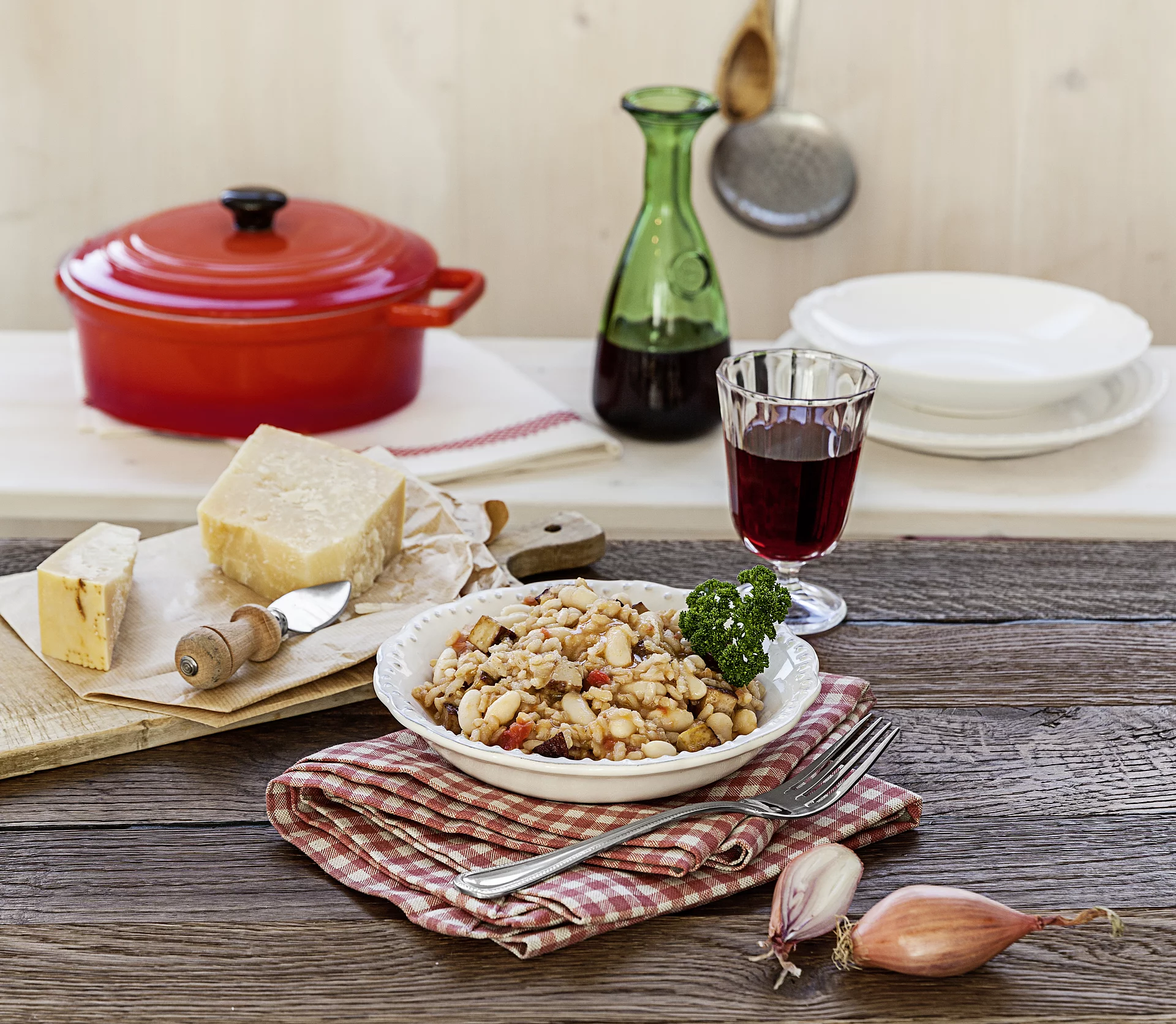 Risotto ist ein echter Klassiker der italienischen Küche. Teller mit Risotto, daneben Käse, Zwiebel, Rotwein, Topf.