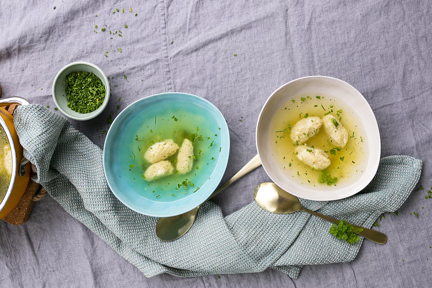 Zwei Teller mit Griesnockerlsuppe mit Klarer Suppe auf einem Tuch.