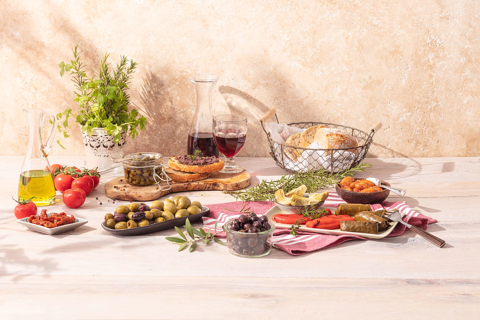 Gedeckter Tisch mit bunter Antipasti-Auswahl wie Dolmas, Oliven, Paprika, Tomaten, Artischocken, dazu Rotwein