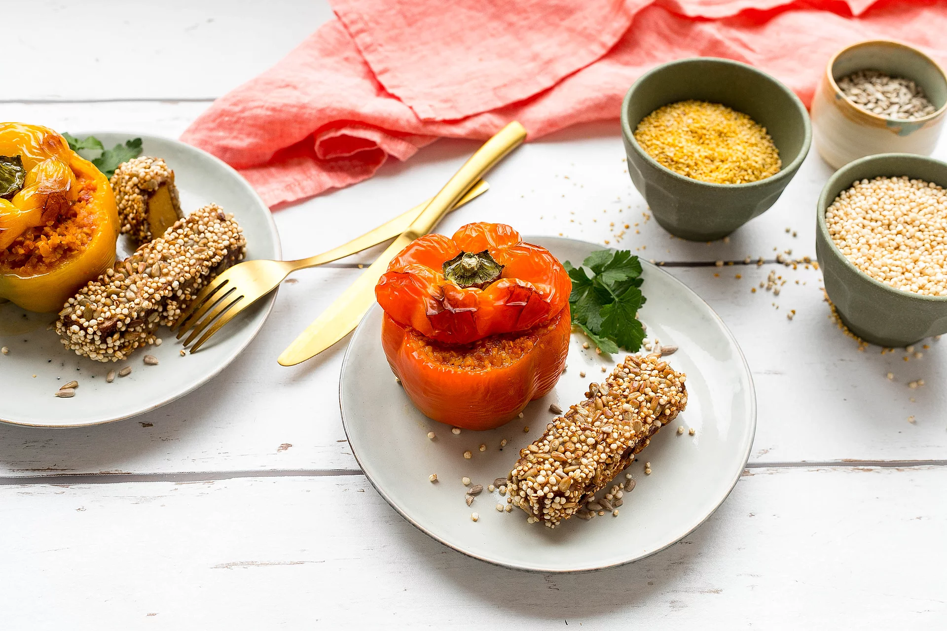Mit Lupinenschrot gefüllte gelbe und orangene Paprika mit Räuchertofu auf Tellern angerichtet.