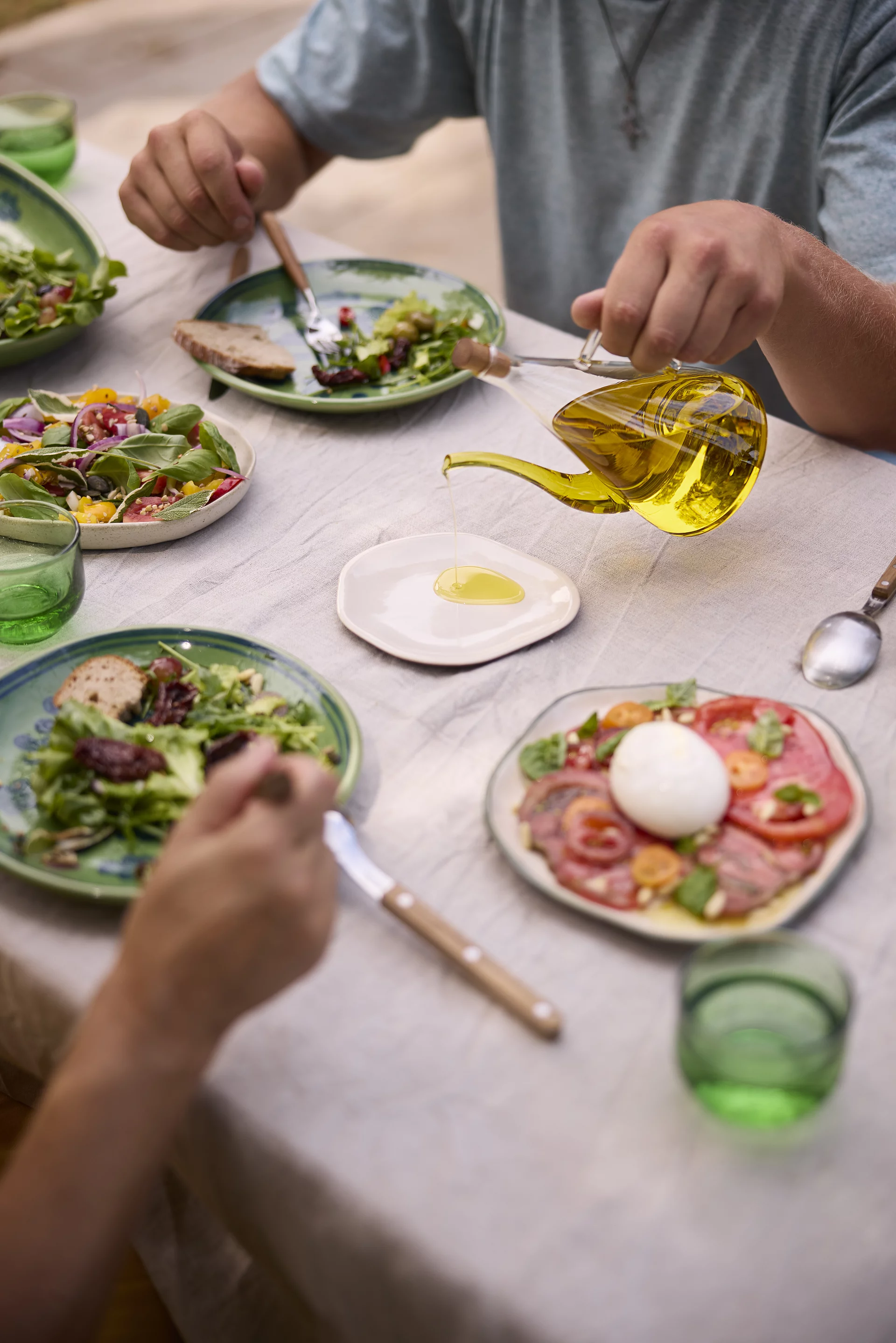 Tisch mit frischen Salatvariationen, Tomaten-Mozzarella und Olivenöl-Dekantierer – Rapunzel Bio-Olivenöl für mediterrane Küche